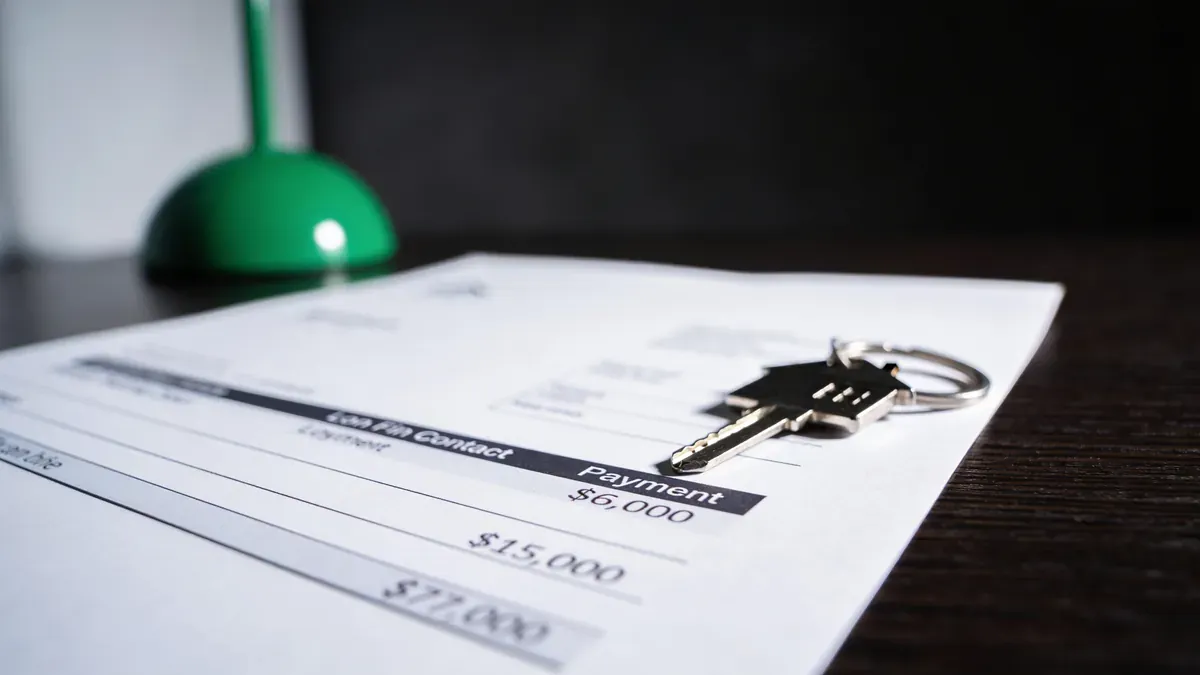 Contrato de financiamento de imóvel com a parcela desfocada e uma chave de casa pousada sobre o papel