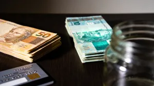 Stack of Brazilian banknotes split into two piles between a credit card and an empty jar, dramatic lighting