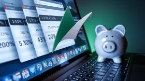 Tela de laptop com abas de comparação financeira, números desfocados, cofrinho cerâmico intocado ao fundo. Luz dramática, contraste alto, destaque em verde esmeralda.
