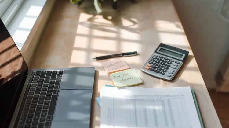 Planilha de controle financeiro aberta em laptop sobre mesa de madeira, com caneta e calculadora simples ao lado, representando organização estruturada.
