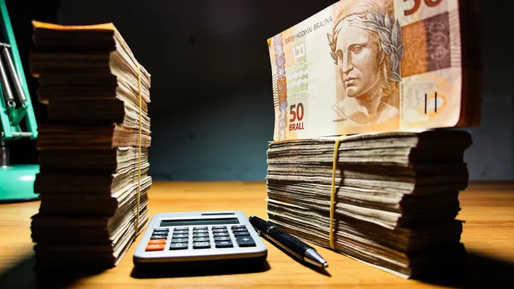 Duas pilhas de notas de real em tamanhos diferentes sobre uma mesa de madeira à noite, uma calculadora e caneta entre elas, iluminação dramática com acento verde esmeralda